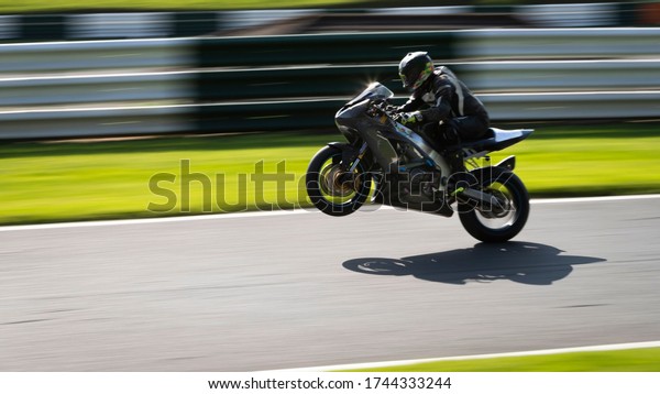 A panning shot of a grey racing bike on one wheel\
as it circuits a track