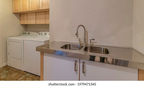 Pano Double Basin Sink And Curved Faucet With Cabinet Inside Functional Laundry Room. Washing Machine, Dryer, And Flush Mount Dome Ceiling Light Can Also Be Seen Inside The Room.