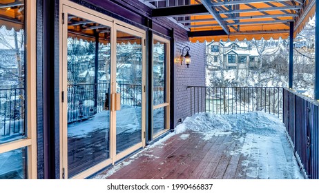 Pano Front Deck Of Building With Double Glass Door And Snow On The Wooden Floor. The Balcony Has Views Of Neighborhood Houses And Frosty Nature Scenery In Winter.