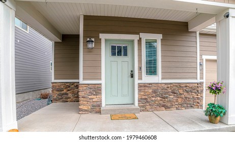 Pano Front Door And Sidelight Against Brick Wall And Wood Siding Of Home With Porch. Steps, Rocky Yard, And Garage Entrance Can Also Be Seen At The Facade Of This House