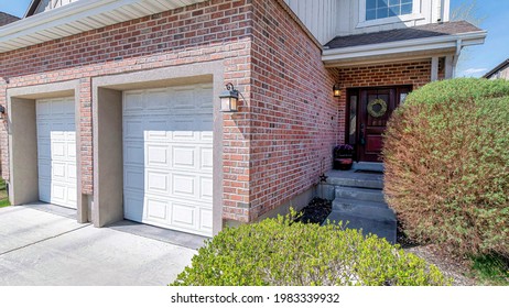 Pano House Facade With Two Car Garage And Front Door With Wreath And Sidelights. Driveway, Landscaped Yard, And Blue Sky Can Also Be Seen In This Sunny Residential Landscape.