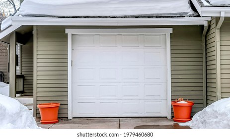 Pano Snowy Driveway And Yard In Winter In Front Of Attached Two Car Garage Of Home. Balconies, Glass Doors, Single Hung Windows, And Gray Wall Can Be Seen At The House Exterior.