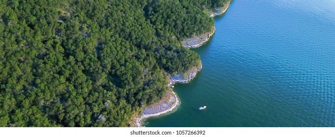 Panorama  Aerial Bluffs With Small Boat At Lake Travis, Austin, Texas, USA. Trees, Cliff Rock Wall Coming Out Of Water From Above. Blue Ocean Crystal, Moderate Wave Looking Straight Down, Green Forest