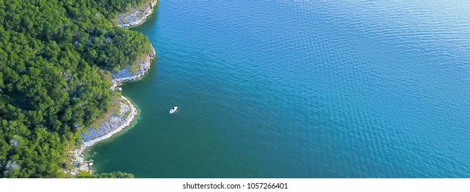 Panorama  Aerial Bluffs With Small Boat At Lake Travis, Austin, Texas, USA. Trees, Cliff Rock Wall Coming Out Of Water From Above. Blue Ocean Crystal, Moderate Wave Looking Straight Down, Green Forest