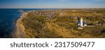 Panorama aerial of lighthouse Hirtshals Fyr with campers and vans parked nearby on the sandy beach and Hirtshals on the background, North Jutland, Denmark, Europe. Hirtshals harbour and ferry.