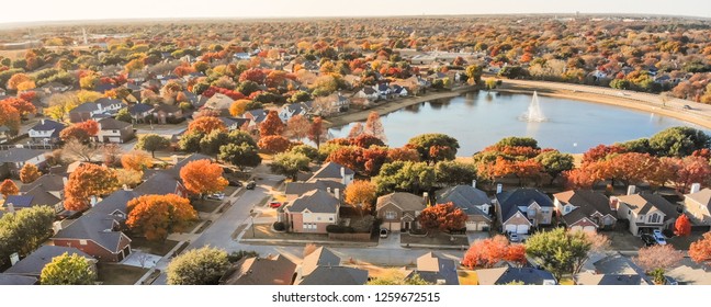 Panorama aerial view lakeside houses neighborhood with colorful autumn leaves. Flyover row of single-family houses with attached garage near lake with water fountain in Flower Mound, Texas, USA