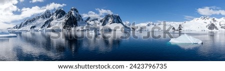 Panorama of Antarctica Landscape with high Rocky Mountains, icebergs, glaciers, clear water with a clear reflection and blue sky 
