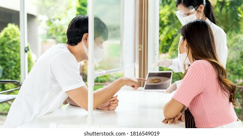 Panorama Asian Waitress Wear Face Mask And Face Shield Using Tablet To Show Restaurant Electronic Menu And Recommend To Couple Customers. New Normal Technology And Lifestyle Food And Dining Concept.