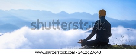Panorama back view of man is relaxingly practicing meditation yoga mudra at mountain top with mist and fog in summer to attain happiness from inner peace wisdom for healthy mind and soul