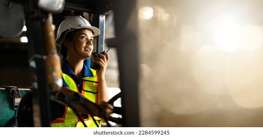 Panorama background banner. 
 Indian woman worker driving a forklift and using a walkie-talkie at warehouse factory container. communication radio. Inventory and wholesale concept - Powered by Shutterstock