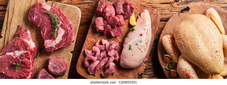 Panorama banner with an assortment of raw meats with a whole chicken, chicken breast, beef and pork on a rustic wooden table