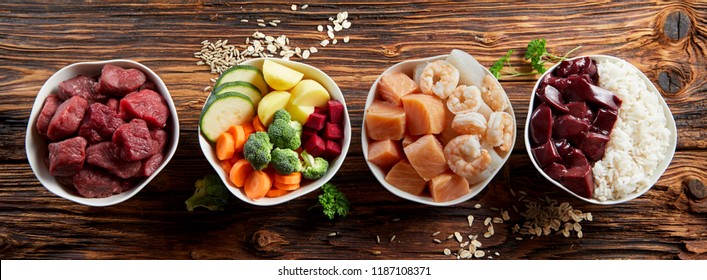 Panorama banner with healthy pet food ingredients with chopped raw beef, liver, chicken, vegetables, rice and grains in individual bowls on rustic wood viewed from above - Shutterstock ID 1187108371