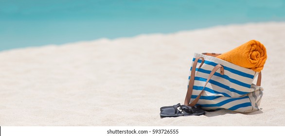 Panorama von Strandtasche, Handtuch und Flip-Flops auf weißem Sand perfekt karibischer Strand mit türkisfarbenem Wasser im Hintergrund auf der anguilla Insel, Urlaubskonzept, Kopienraum auf der linken Seite