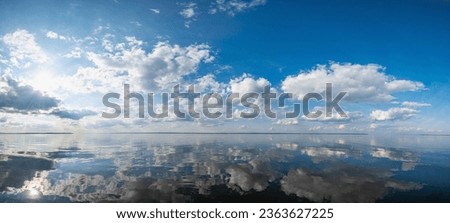 Panorama of the calm mirrored Kama River in Russia, Perm Krai, blue sky with clouds and the sun reflected in the water.