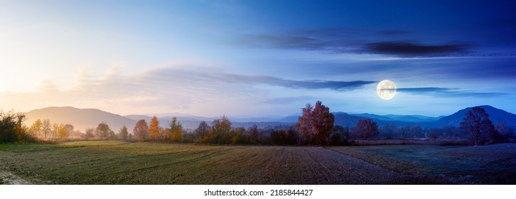 panorama of a carpathian rural landscape at twilight. arable in front of a forest in colorful foliage. day and night time change concept. distant mountains beneath a sun and moon. hazy atmosphere - Shutterstock ID 2185844427
