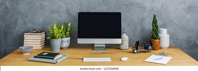 Panorama Close-up Of A Simple Workspace Interior With A Computer, Plants, Books And Notes On A Wooden Desk By A Gray Wall. Place For Your Graphic