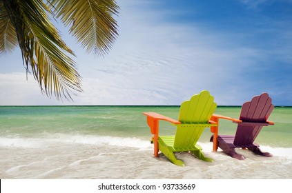 Panorama of colorful lounge chairs at a tropical paradise beach in Miami Florida. Beautiful aqua green waters of the ocean, hanging palm tree branches  and a blue sky in the background