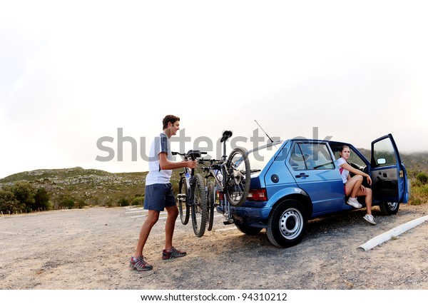 Panorama of a couple\
who have finished mountain biking outdoors and are loading the\
bicycles onto the car bike rack. large image, lots of copyspace,\
healthy lifestyle\
scene.