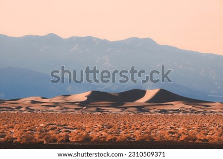 Panorama of dramatic light and shadow over desert landscape of the golden Mesquite flat sand dunes against the rugged badlands terrain in Death Valley National Park, USA.