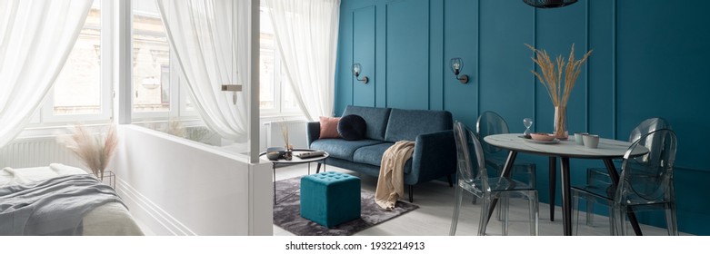 Panorama of elegant and small living room with dining area ane with teal blue wall with molding next to bedroom behind white and glass wall - Shutterstock ID 1932214913
