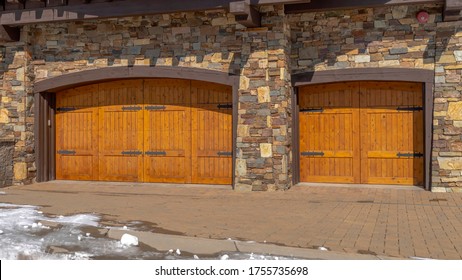 Panorama Facade Of Home Featuring Two Hinged Wooden Garage Doors And Stone Brick Wall