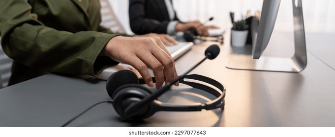 Panorama focus hand holding headset on call center workspace desk with blur background of operator team or telesales representative engaging in providing client with customer support service. Prodigy - Powered by Shutterstock