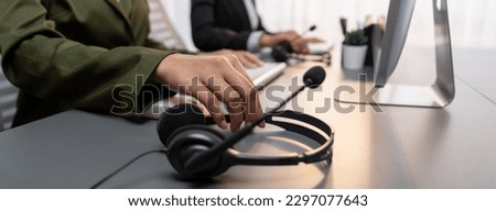 Panorama focus hand holding headset on call center workspace desk with blur background of operator team or telesales representative engaging in providing client with customer support service. Prodigy