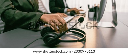 Panorama focus hand holding headset on call center workspace desk with blur background of operator team or telesales representative engaging in providing client with customer support service. Prodigy