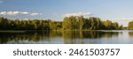Panorama of a forest lake. View of trees on the shore of the lake. Beautiful summer landscape. Ecological tourism and outdoor recreation.