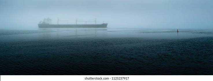 Panorama Of A Freight Ship Travelling On A River Near A Marker Bouy During A Foggy Morning.