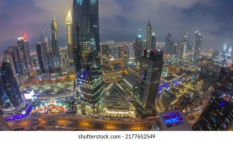 Panorama Of Futuristic Skyscrapers After Sunset In Financial District Business Center In Dubai With Traffic On A Road Day To Night Transition Timelapse. Aerial View From Above With Cloudy Sky