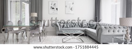 Panorama of glamour designed living room in white and gray with elegant quilted corner sofa and glass dining table