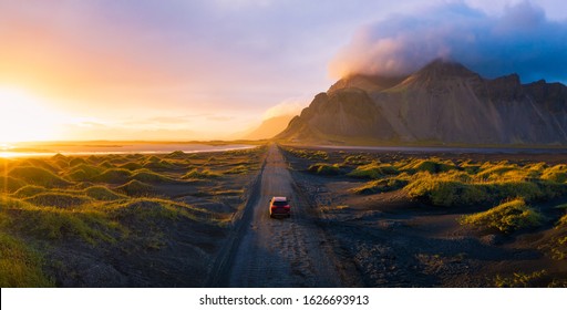 Panorama of a gravel road at a golden Sunset with Vestrahorn mountain in the background and a car driving the road in Iceland