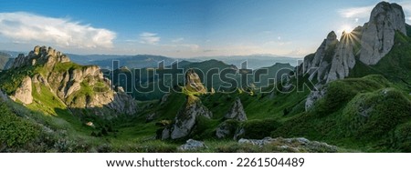
Panorama of green meadow with rocks and rocky mountains in romanian mountains in muntii ciucas with setting sun