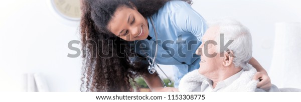 Panorama of happy caregiver supporting smiling\
elderly man in the nursing\
house