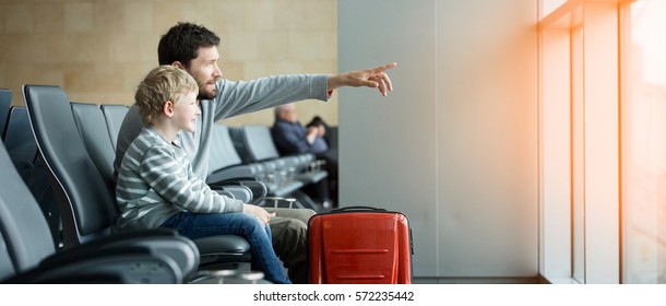 Panorama der glücklichen Familie von zwei, Vater und Sohn, warten zusammen auf dem Flughafen für den Flug mit Gepäck, Vater mit Finger auf etwas, Sonnenfleckeneffekt