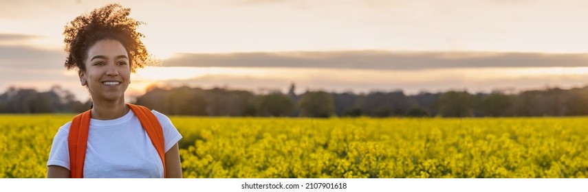 Panorama header beautiful biracial African American girl teenager female young woman smiling and happy hiking with back pack in a field of yellow flowers at sunset or sunrise panoramic web banner. - Powered by Shutterstock