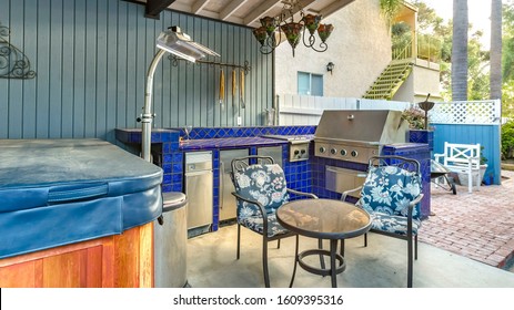 Panorama High angle view of a stylish outdoor kitchen on a brick patio with a built in gas barbecue,rug and dining table with hanging chandelier