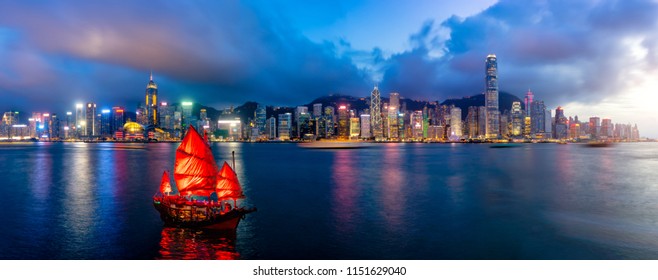 Panorama of Hong Kong City skyline with tourist sailboat at night. View from across Victoria Harbor HongKong.