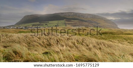 Panorama image of Knocknarea hill and Strandhill town in county Sligo, Ireland. cloudy sky, Green field with tall grass in foreground. Nobody.