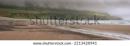 Panorama image of stunning nature scenery and Keem beach, county Mayo, Ireland. Popular travel area with surfing and sightseeing. Irish landscape. Low clouds, rainy day. Stormy weather.