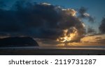 A panorama image of a sun burst at sunset and Tillamook Head headland and the beach at Seaside Oregon.