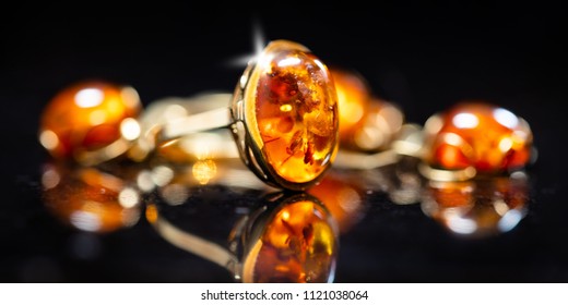 panorama of jewelry with amber stones, amber necklace ring and earring and pendant with noble metal like gold, in front of a black background on a black stone with reflection