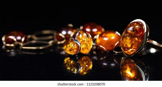 panorama of jewelry with amber stones, amber necklace ring and earring and pendant with noble metal like gold, in front of a black background on a black stone with reflection