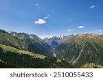 Panorama of Karakol Gorge. Summer natural landscape. Mountain range, dense coniferous forest and snow capped peaks. Travel destination in Kyrgyzstan, Kirgiziya Mountains. Scenery, hight point of view