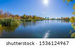 Panorama of a lake in Autumn on October 19th 2019 in Nuns Island, Montreal, Quebec, Canada. The forest is full of autumn colored trees and we can see buildings in the background.