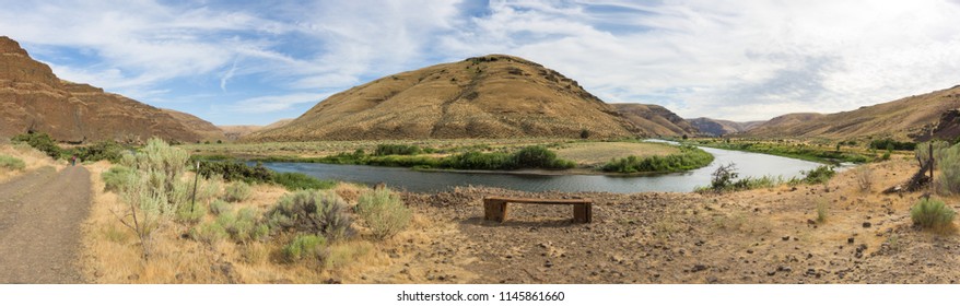 Panorama Landscape Of Cottowood Canyon State Park, Oregon, With Mountains Reflecting In A River And Rock Formations.