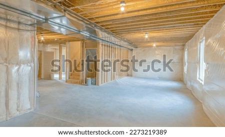 Panorama Large unfinished basement with woodframes and wall insulation. Basement interior with plastic vapor barrier and windows on the left side.