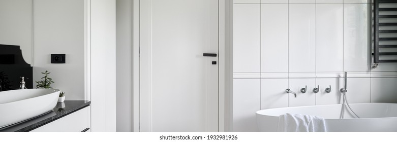 Panorama of luxury black and white bathroom with freestanding bathtub, stylish washbasin and white doors with black handle