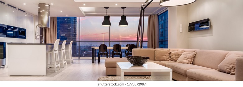 Panorama of luxury decorated living room with kitchen in apartment with big window wall during sunset - Shutterstock ID 1773572987
